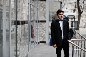 Young indian man on black suit and bow tie posed outdoor. Luxury suits Fifth Avenue